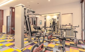 Un gimnasio con equipos de ejercicio variados, suelo a cuadros y un espejo que refleja el equipo.