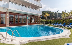 A hotel with a swimming pool, lounge chairs, and a building with multiple floors.