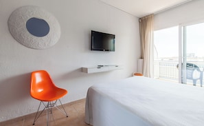 A hotel room with a bed, a television, a white wall, a round decorative wall piece, and a window with curtains. - BLUESEA Montevista Hawai (Lloret de Mar)