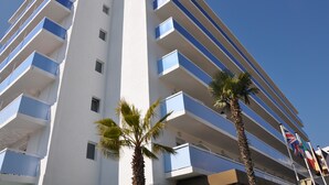 A modern hotel with multiple balconies, palm trees, and flags. - BLUESEA Montevista Hawai (Lloret de Mar)