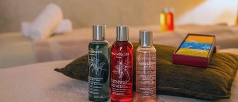 Three bottles of Cinq Mondes Paris on a beige towel with a pillow and a red box in the background.