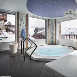 Relax in a serene spa area with a large hot tub, surrounded by a spacious room with high ceilings and stunning mountain views.