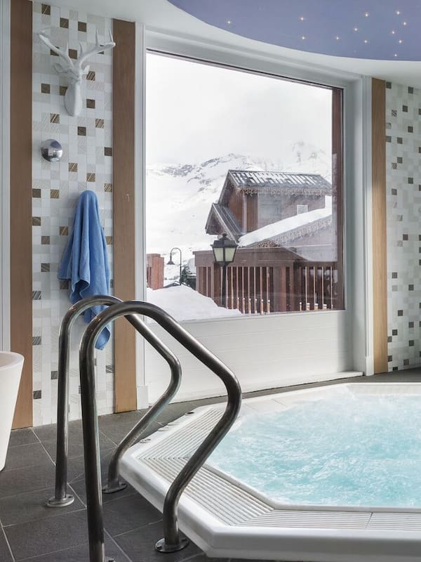 Relax in a serene spa room with a large hot tub, surrounded by a stunning mountain view and a deck.