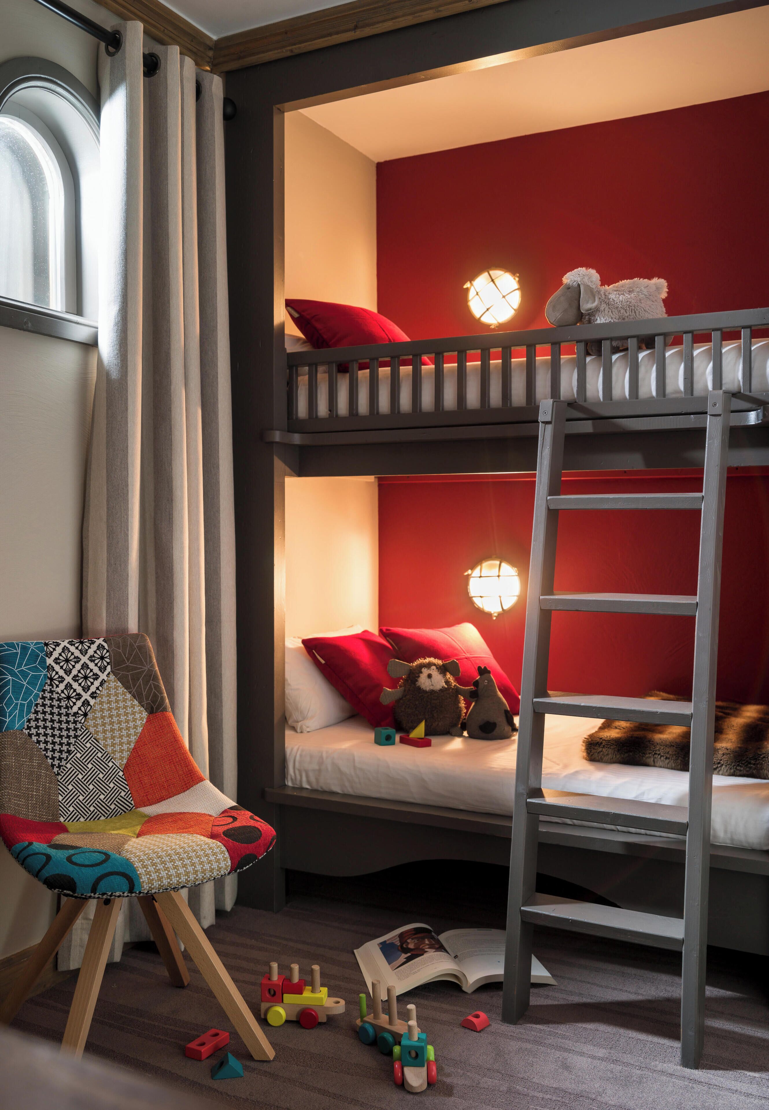 A bunk bed room with a ladder, a chair, and toys on the floor.