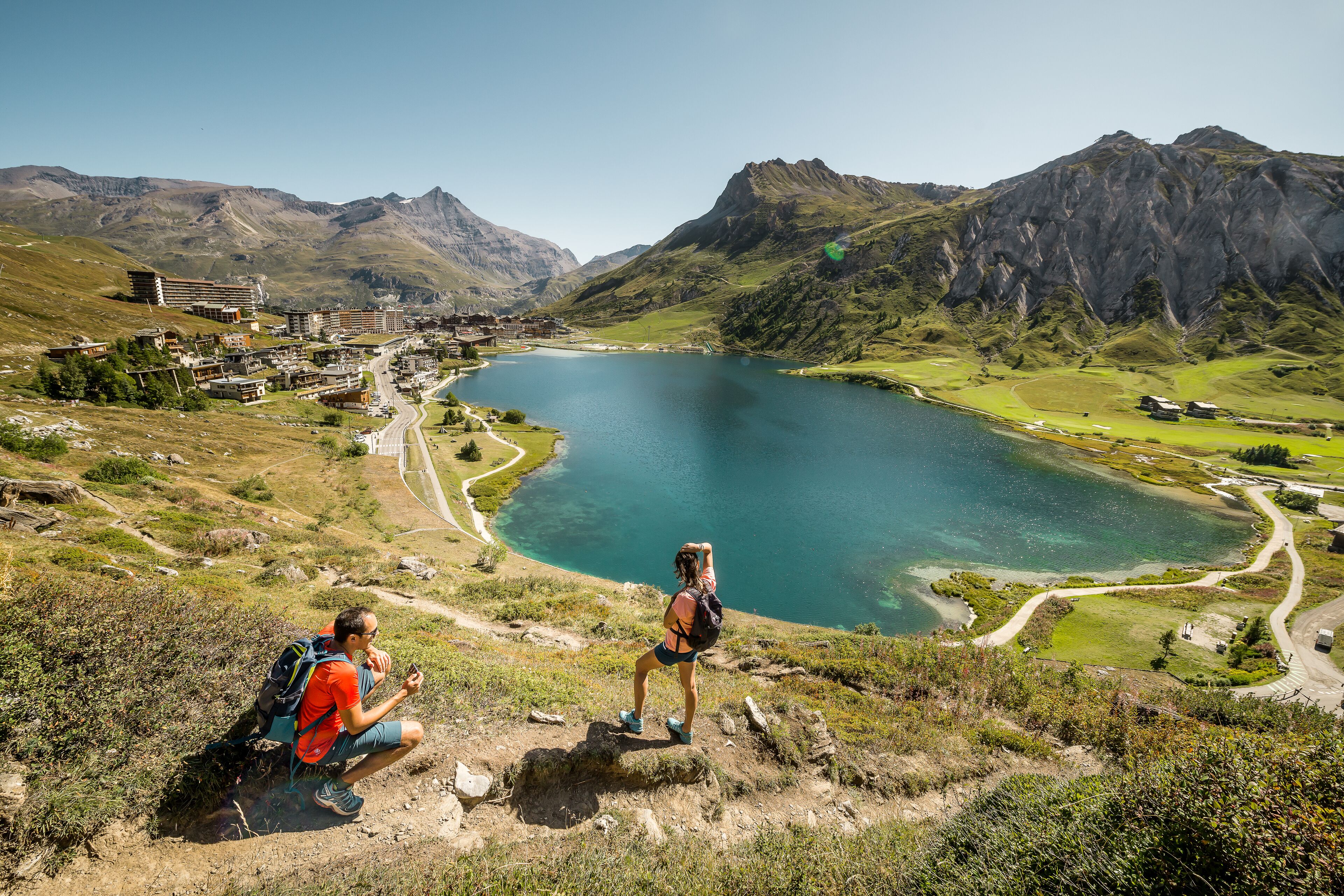 Un paysage montagneux avec un lac, une petite ville et un sentier de randonnée.
