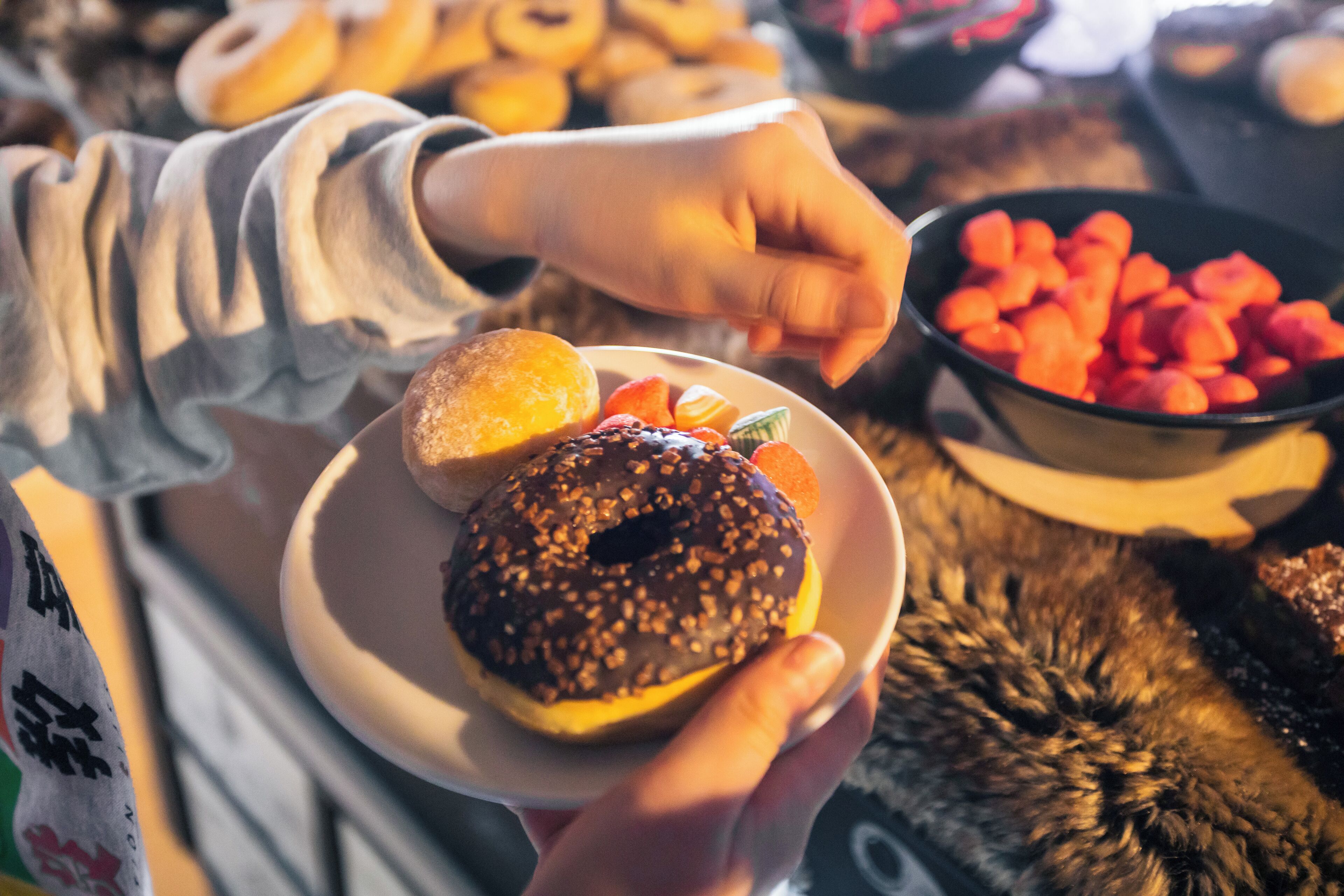 Une personne tenant une assiette avec un beignet au chocolat et un biscuit, et, à l’arrière-plan, un bol rempli de tranches d’orange.