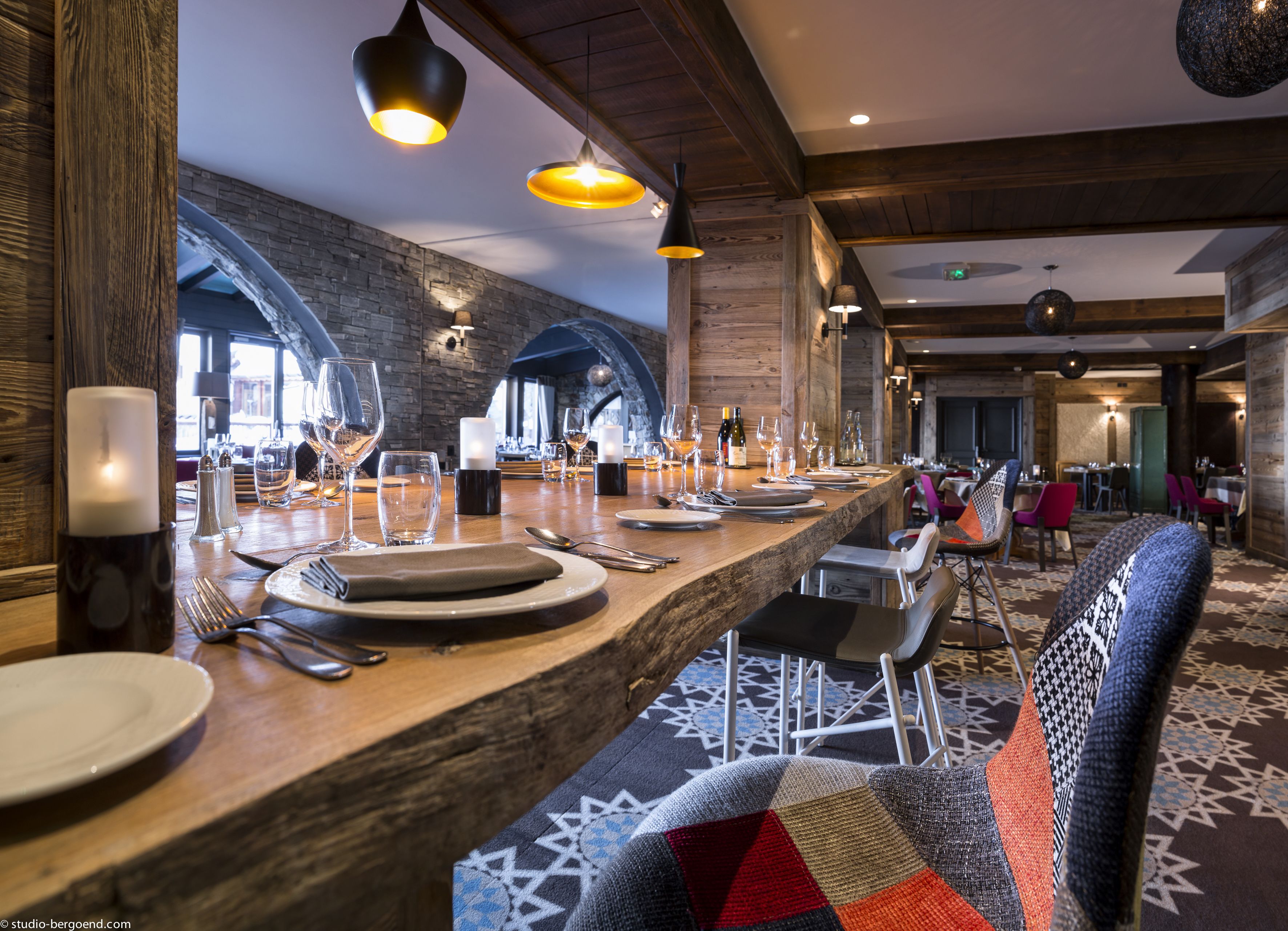 A restaurant with a long wooden bar, multiple tables set for dining, and a patterned carpet.