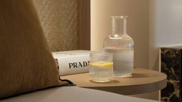 A neatly arranged hotel room with a bed, a bedside table with a lamp, a bottle, and a glass.