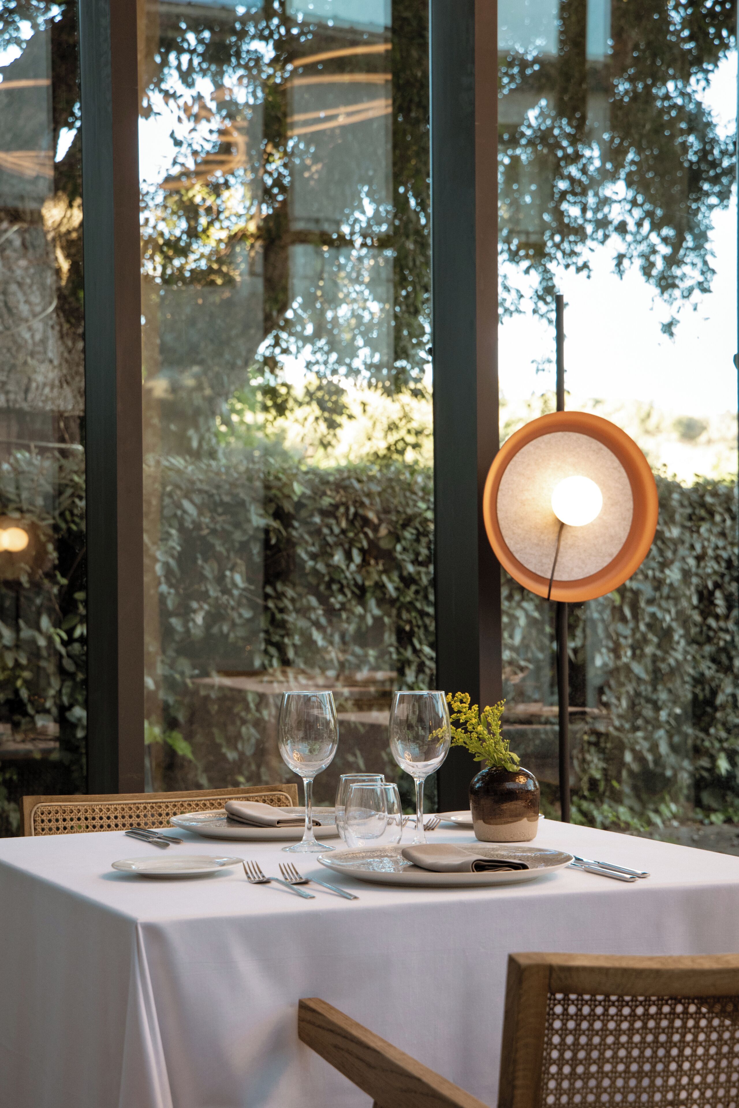 A table set for dining with a view of greenery through large windows.