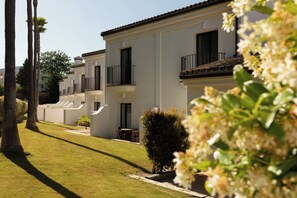 A row of white buildings with balconies, a well-maintained lawn, and a small table and chair set outside. - Hotel Encinar de Sotogrande (San Roque)
