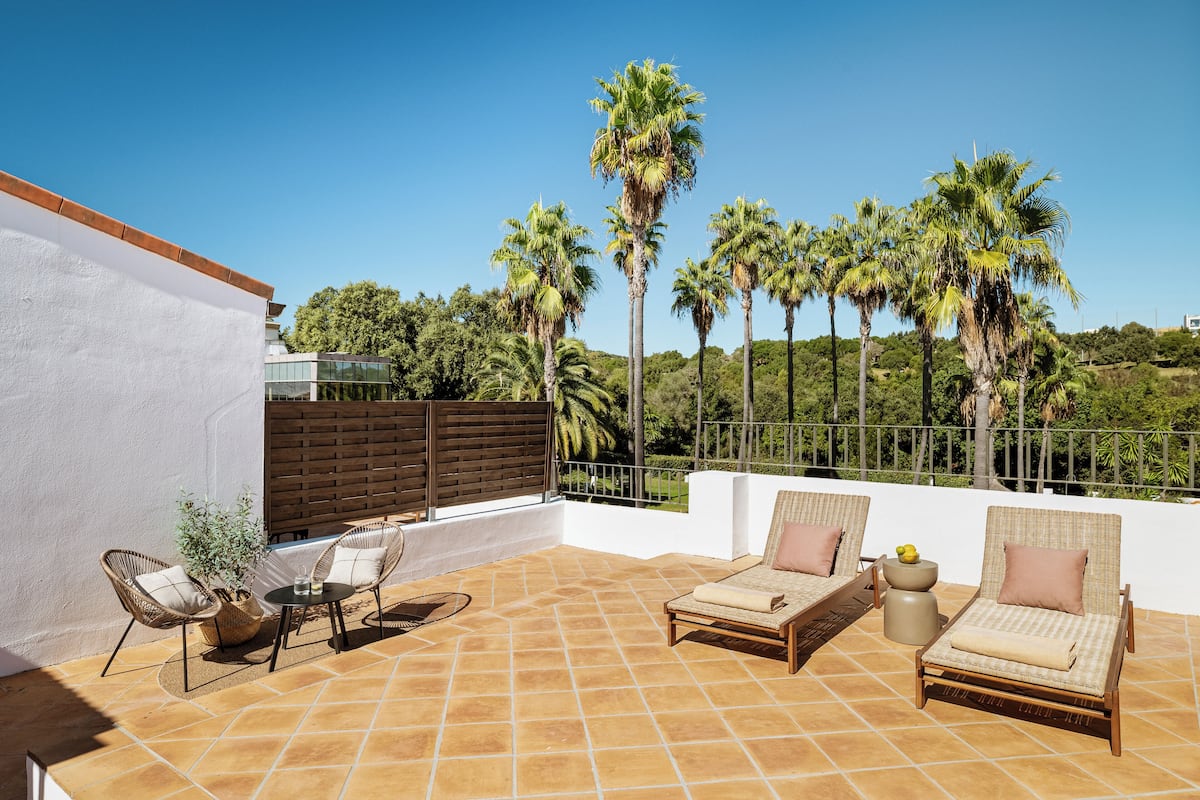 An outdoor patio with two wicker lounge chairs, a small table, and a potted plant.