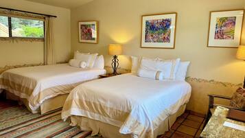 Habitación de hotel con dos camas, una ventana con cortinas, una alfombra estampada y cuadros en las paredes.