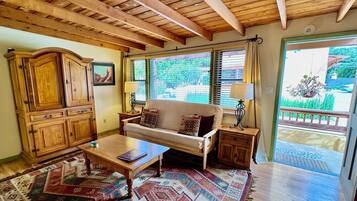 A cozy living room with a wooden ceiling, a sofa, a coffee table, and a large window with blinds.
