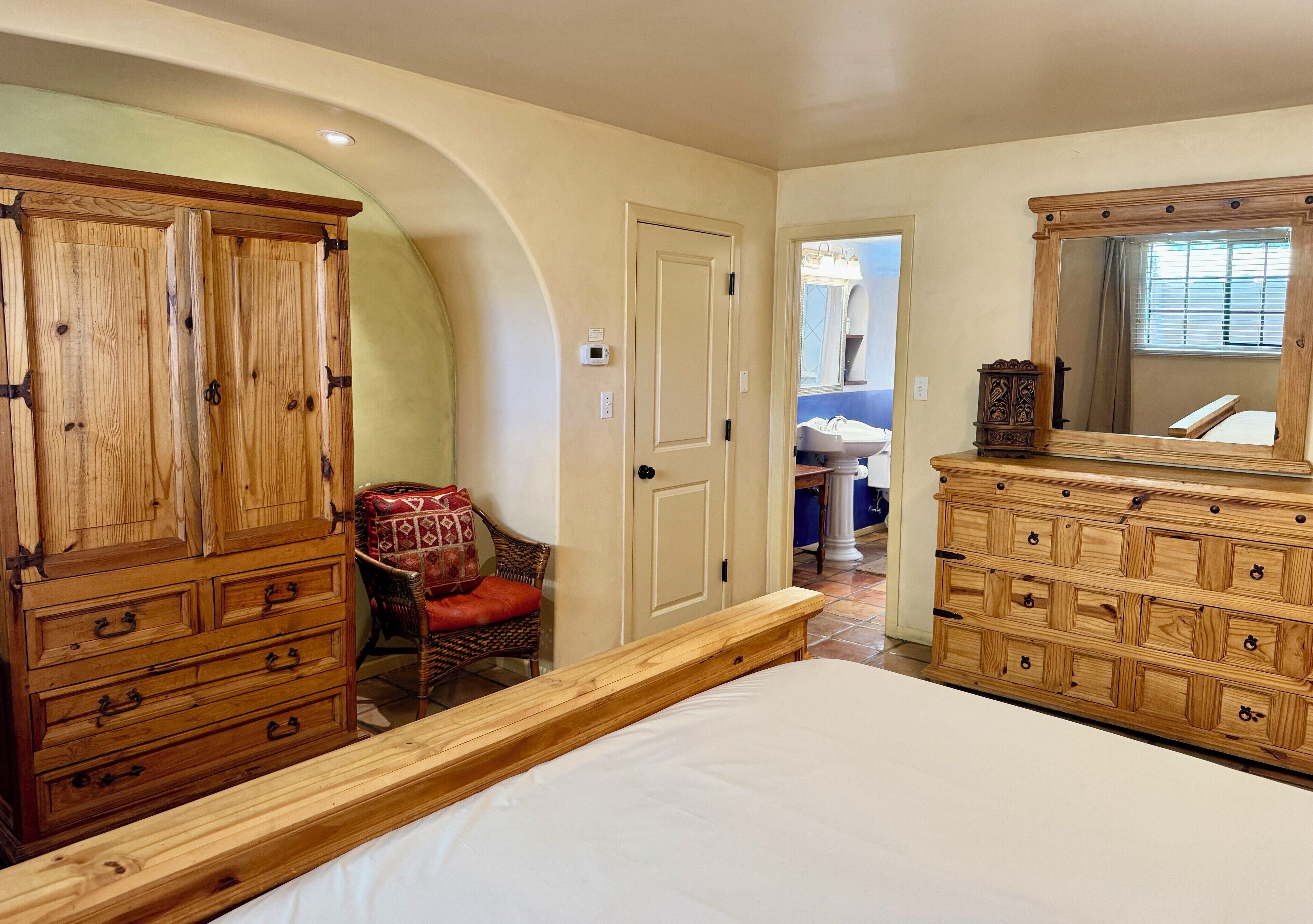 A bedroom with a large bed, wooden dressers, a chair, and a door leading to another room.