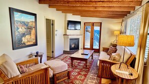 A cozy living room with a fireplace, wooden furniture, a large painting, and a view through the door. - Blue Iguana Inn (Ojai)