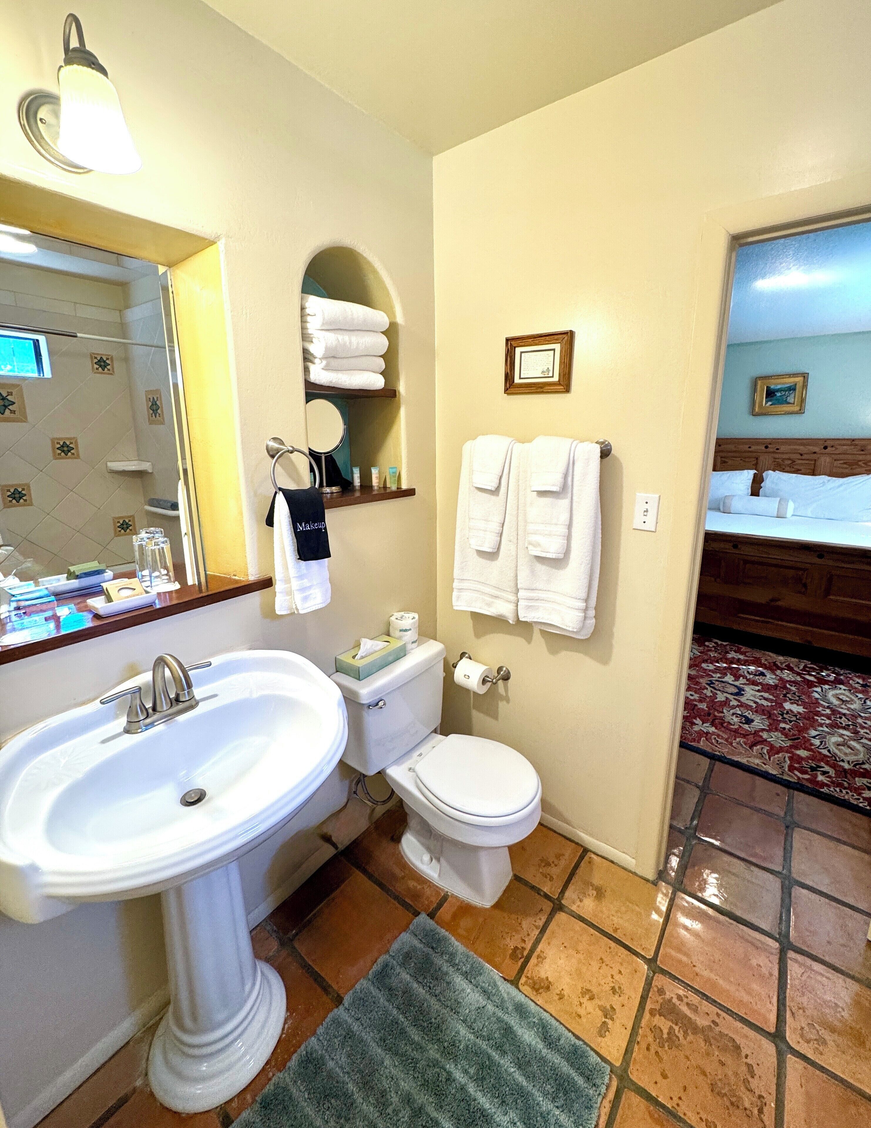 A bathroom with a sink, toilet, and a mirror. There are towels and toiletries on the wall.