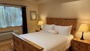 A bedroom with a wooden bed, two bedside tables with lamps, a ceiling fan, a window with blinds, and a radiator.