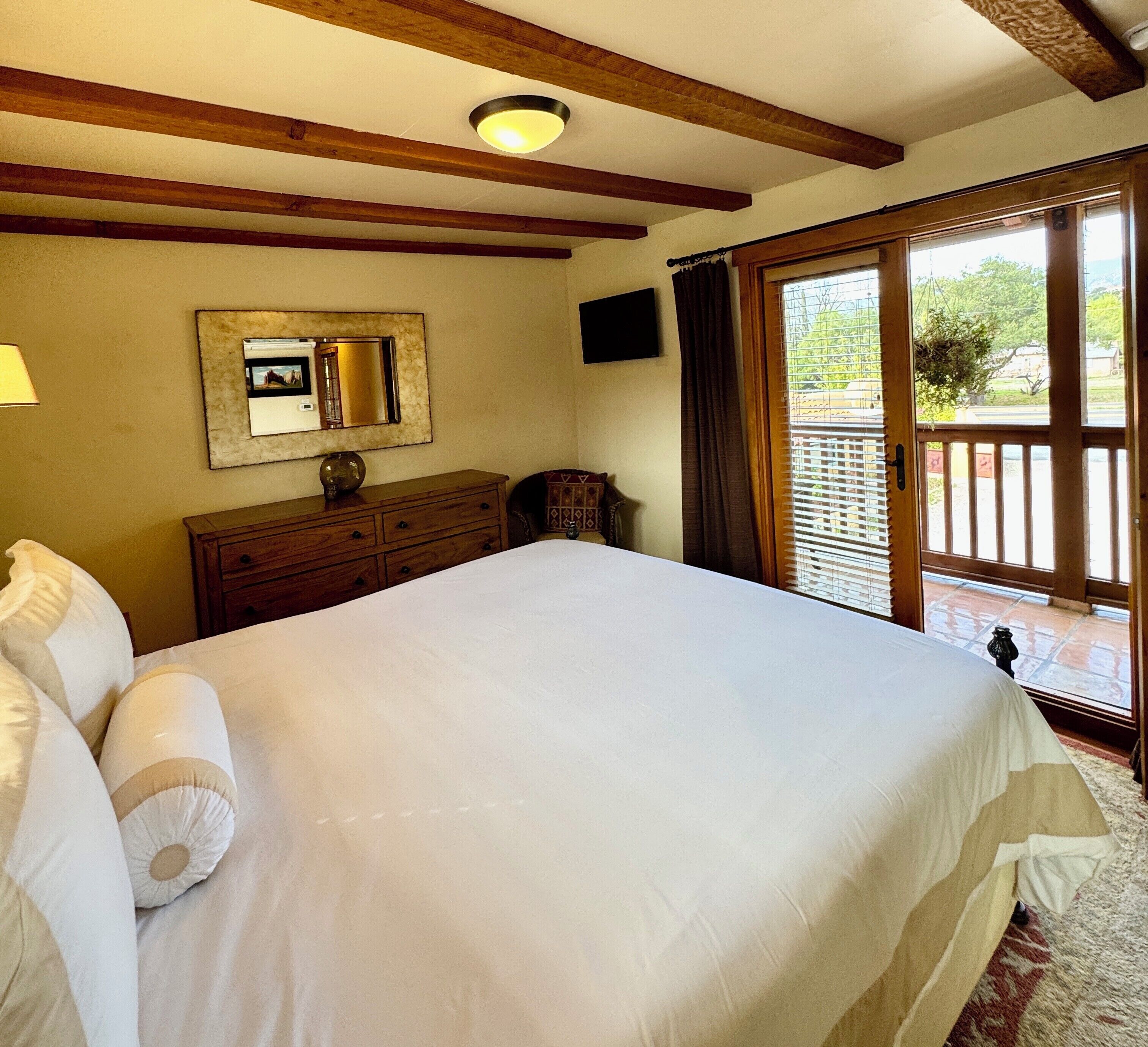 Un dormitorio con una cama grande, vigas de madera, un aparador, un espejo y vistas al exterior a través de una puerta corrediza.
