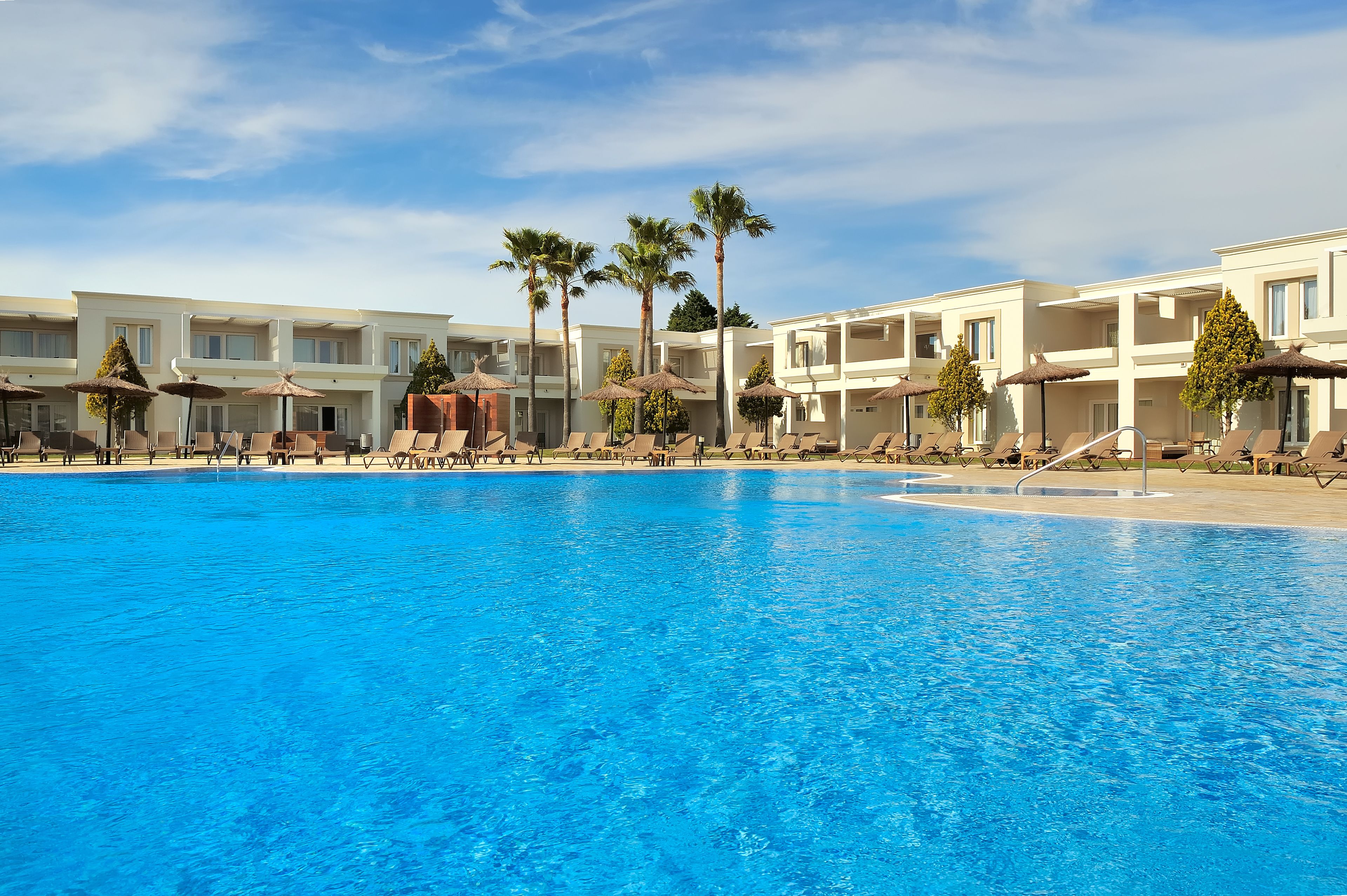 A pool area with lounge chairs and umbrellas, surrounded by multi-story buildings with balconies.