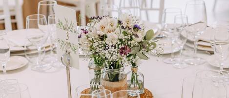 Une table dressée pour un événement formel, avec des nappes blanches, de la verrerie et un centre de table floral.