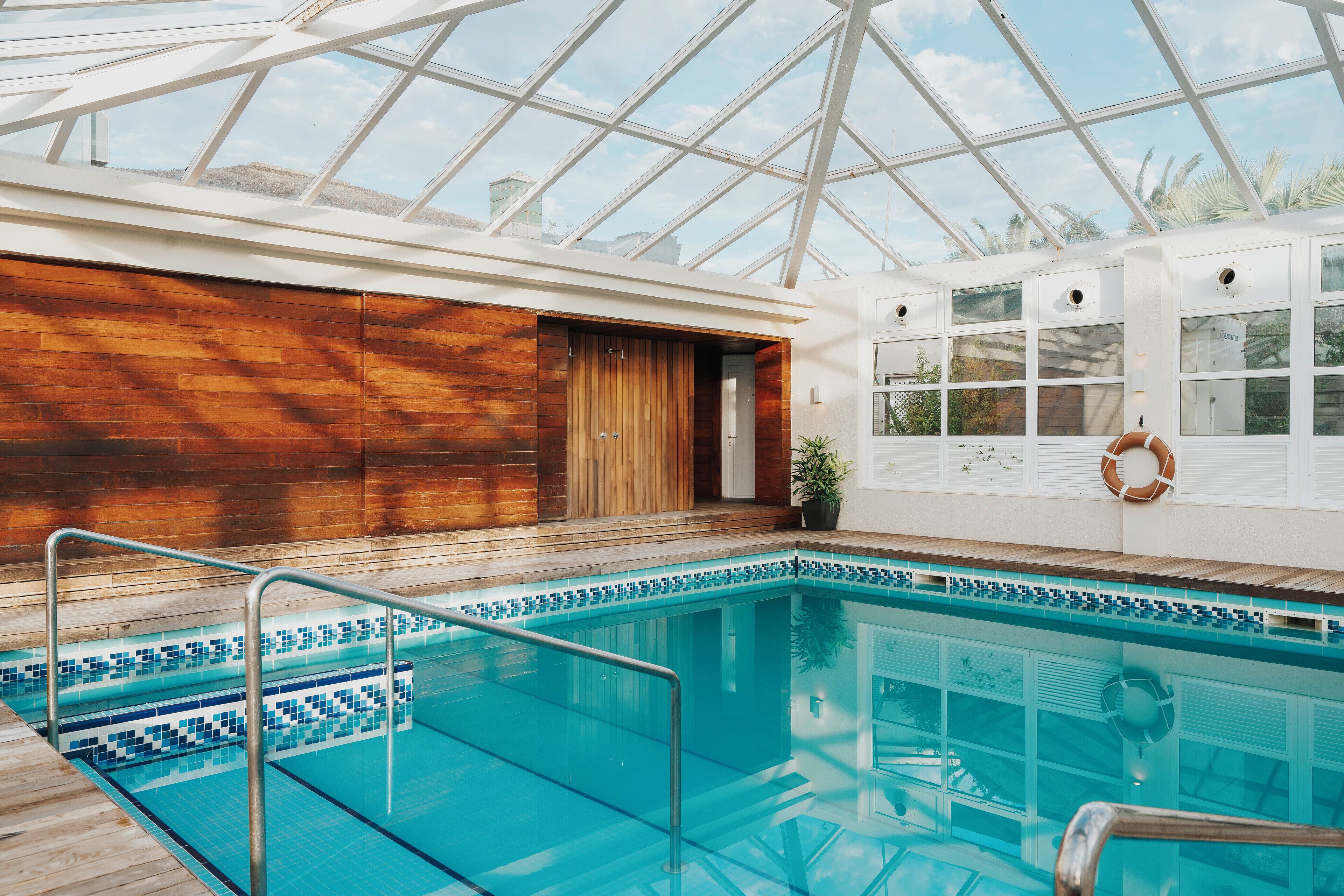 A swimming pool with a glass ceiling, wooden walls, and a lifebuoy on the wall.