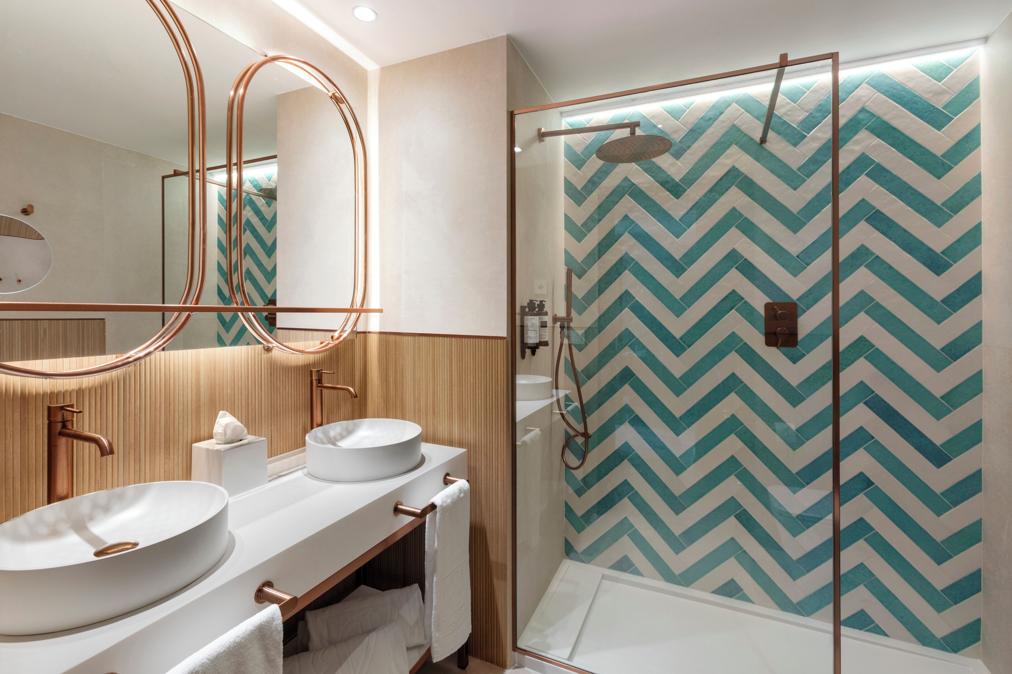 A modern bathroom with two sinks, a mirror, and a shower with a chevron-patterned wall.