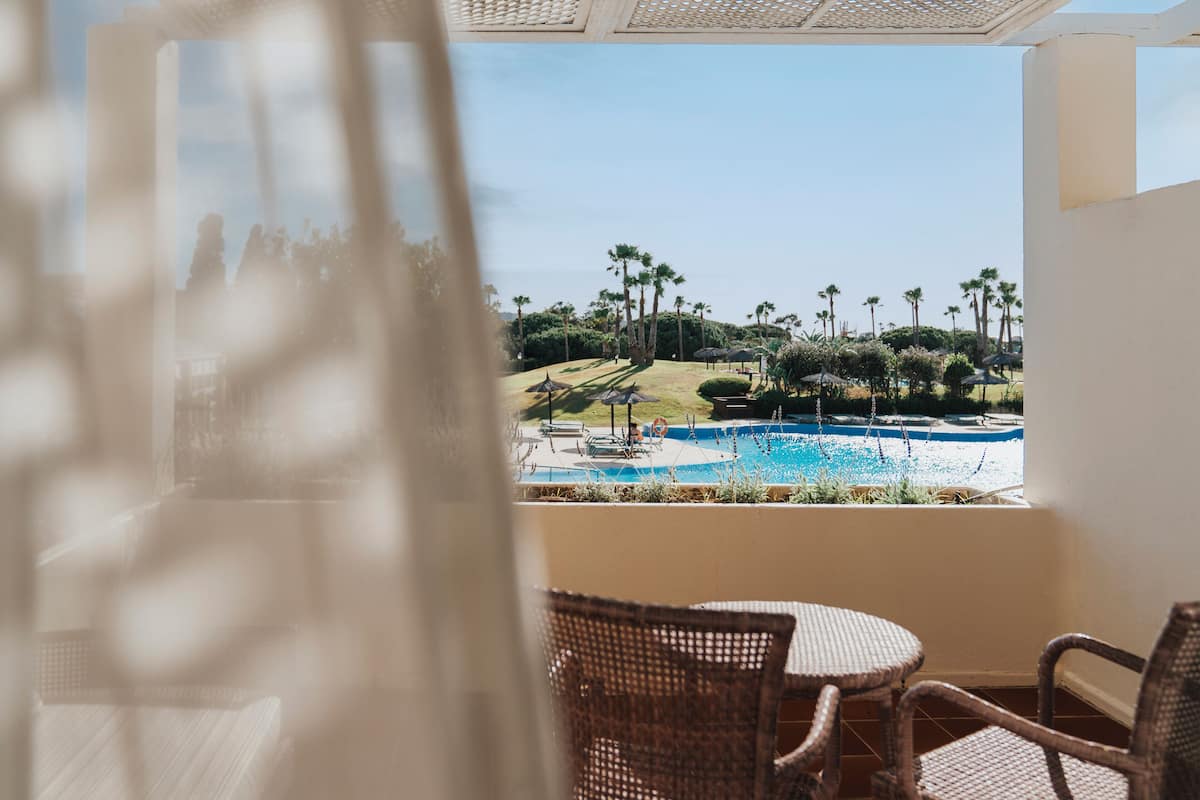 A view of a swimming pool with palm trees and a clear sky.