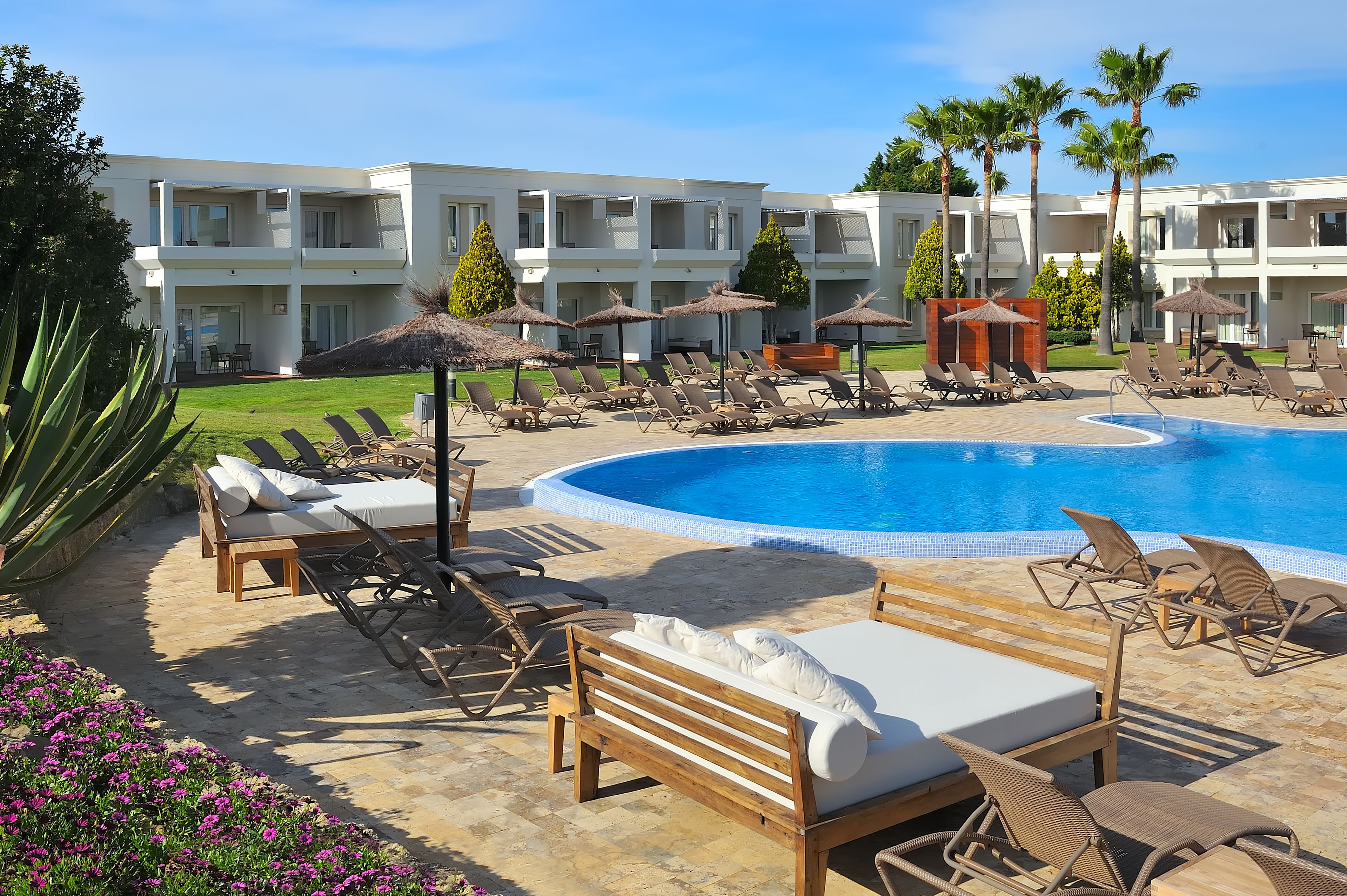 A resort with a swimming pool, sun loungers, and a building with multiple balconies.