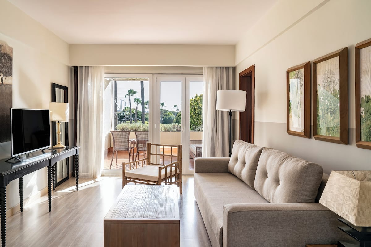 A modern living room with a sofa, a TV on a stand, a coffee table, and a balcony with a chair and table.