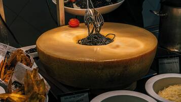 A cheese wheel with a cheese slicer above it, surrounded by various food items and condiments.