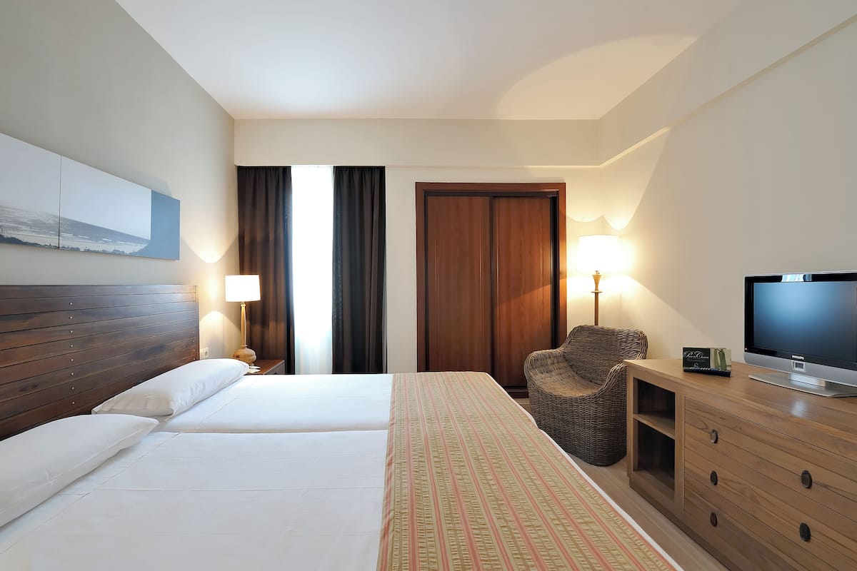 Habitación de hotel con dos camas, televisión, silla, escritorio y lámpara.