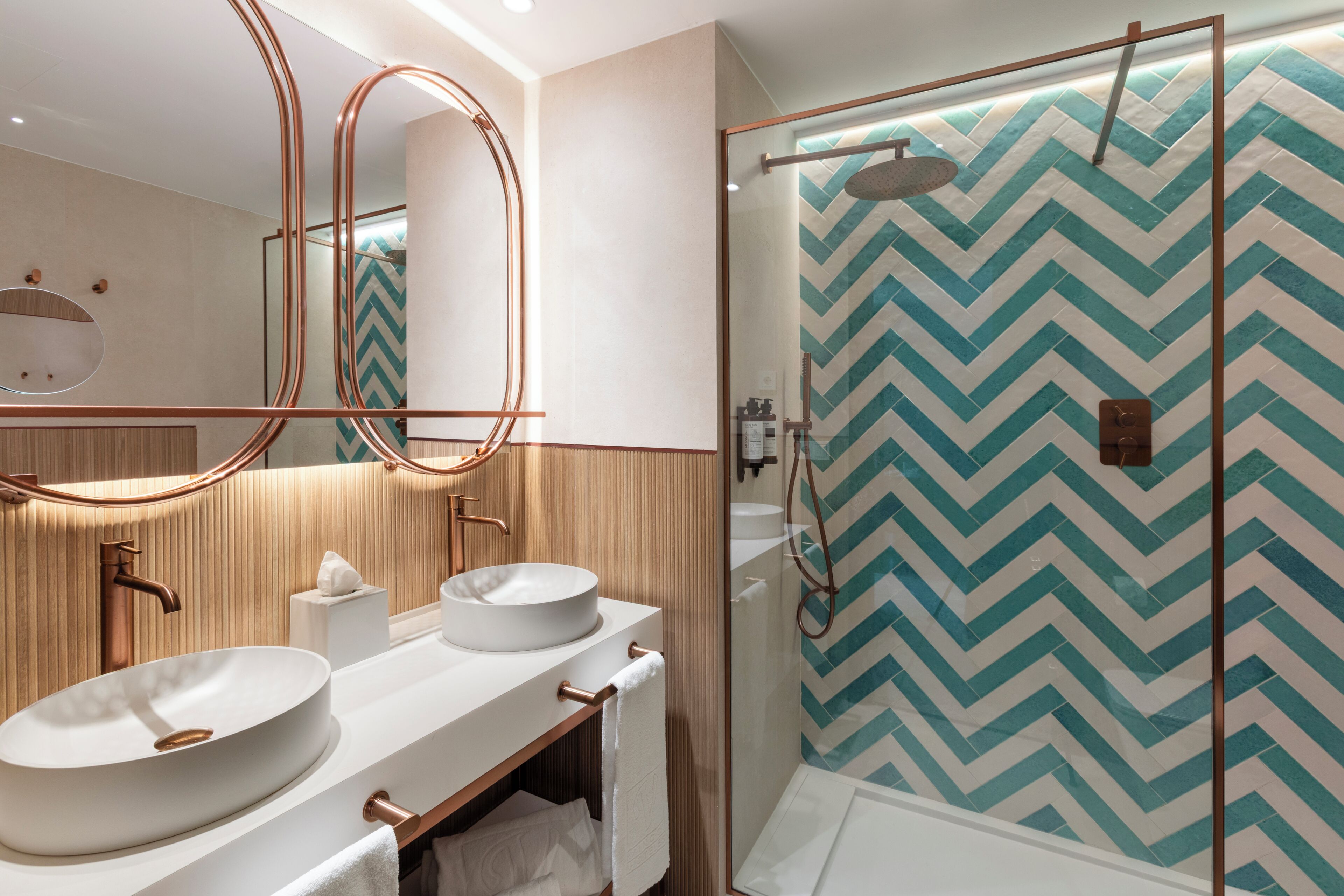 A modern bathroom with two sinks, a large mirror, and a shower area with a chevron-patterned wall.