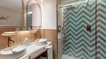 A modern bathroom with two sinks, a large mirror, and a shower area with a chevron-patterned wall.