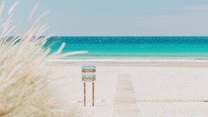 Una playa con un muelle de madera que lleva a un letrero.