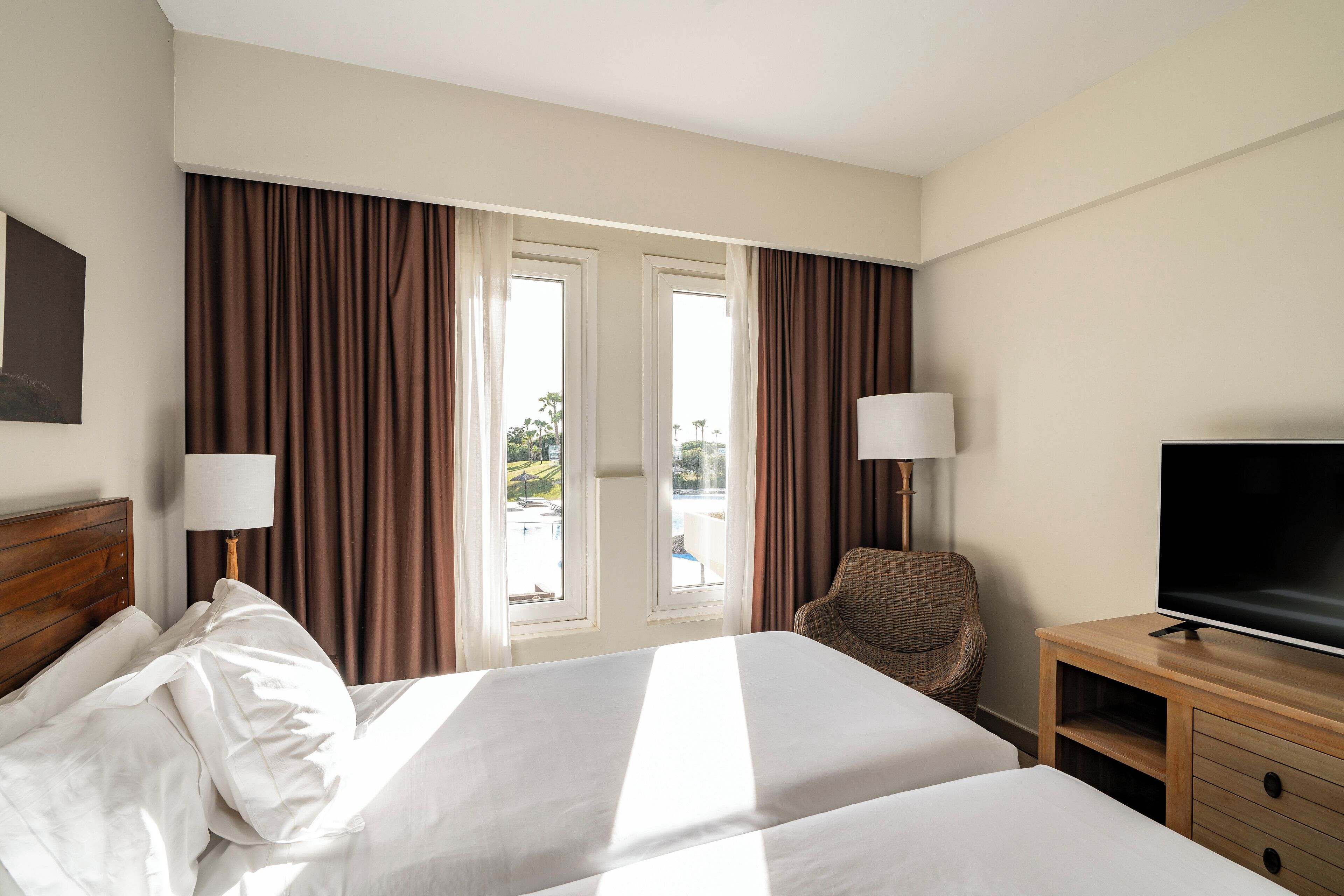 Habitación de hotel con dos camas, televisión, una silla y vistas al exterior.