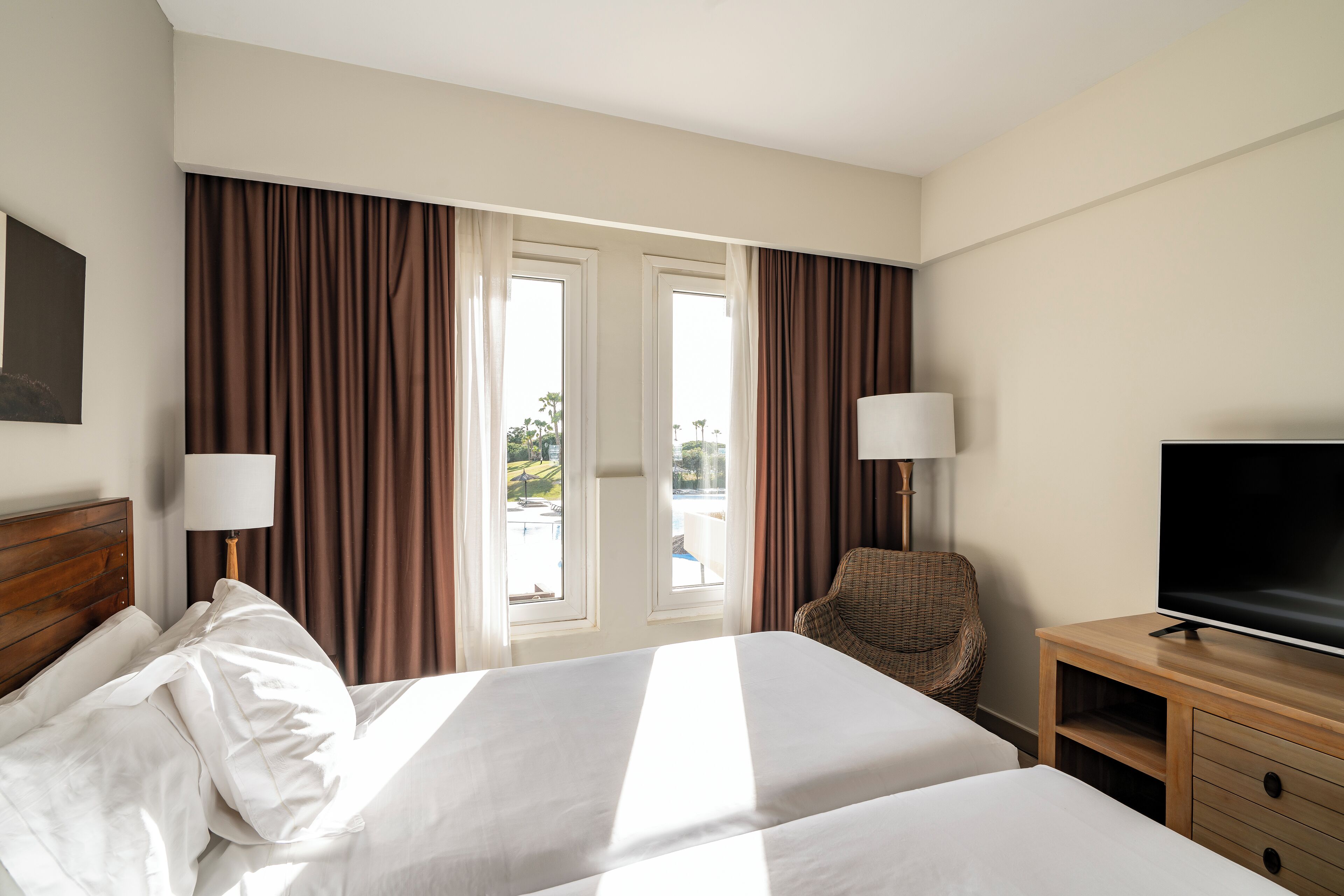 A hotel room with two beds, a television, a chair, and a view of the outdoors.