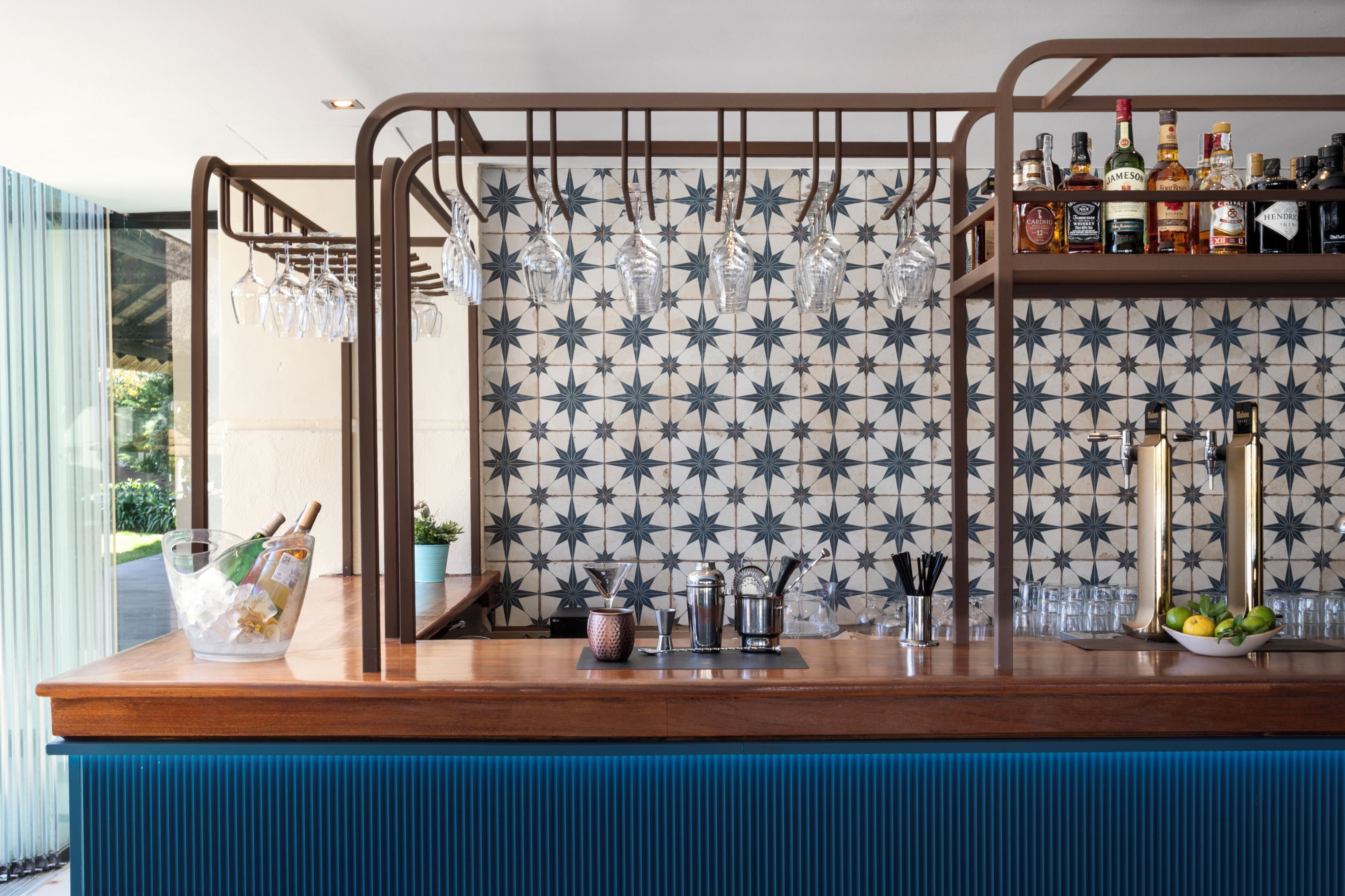 A bar area with a patterned wall, hanging glasses, bottles, and a blue counter.