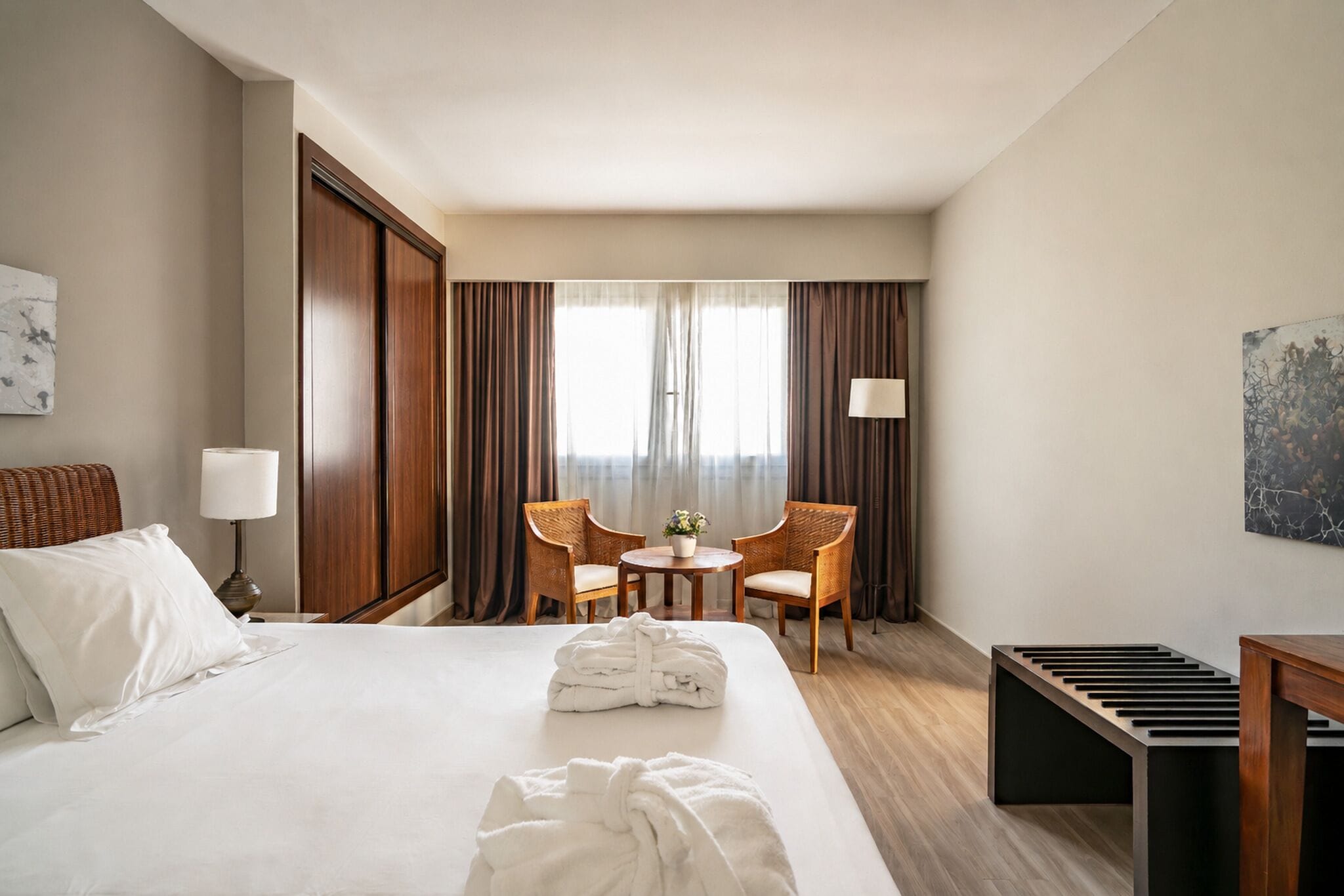 A hotel room with a large bed, two chairs, a small table, and a lamp.