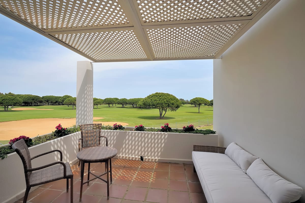 A balcony with a view of a golf course, wicker chairs, a white sofa, and a pergola.