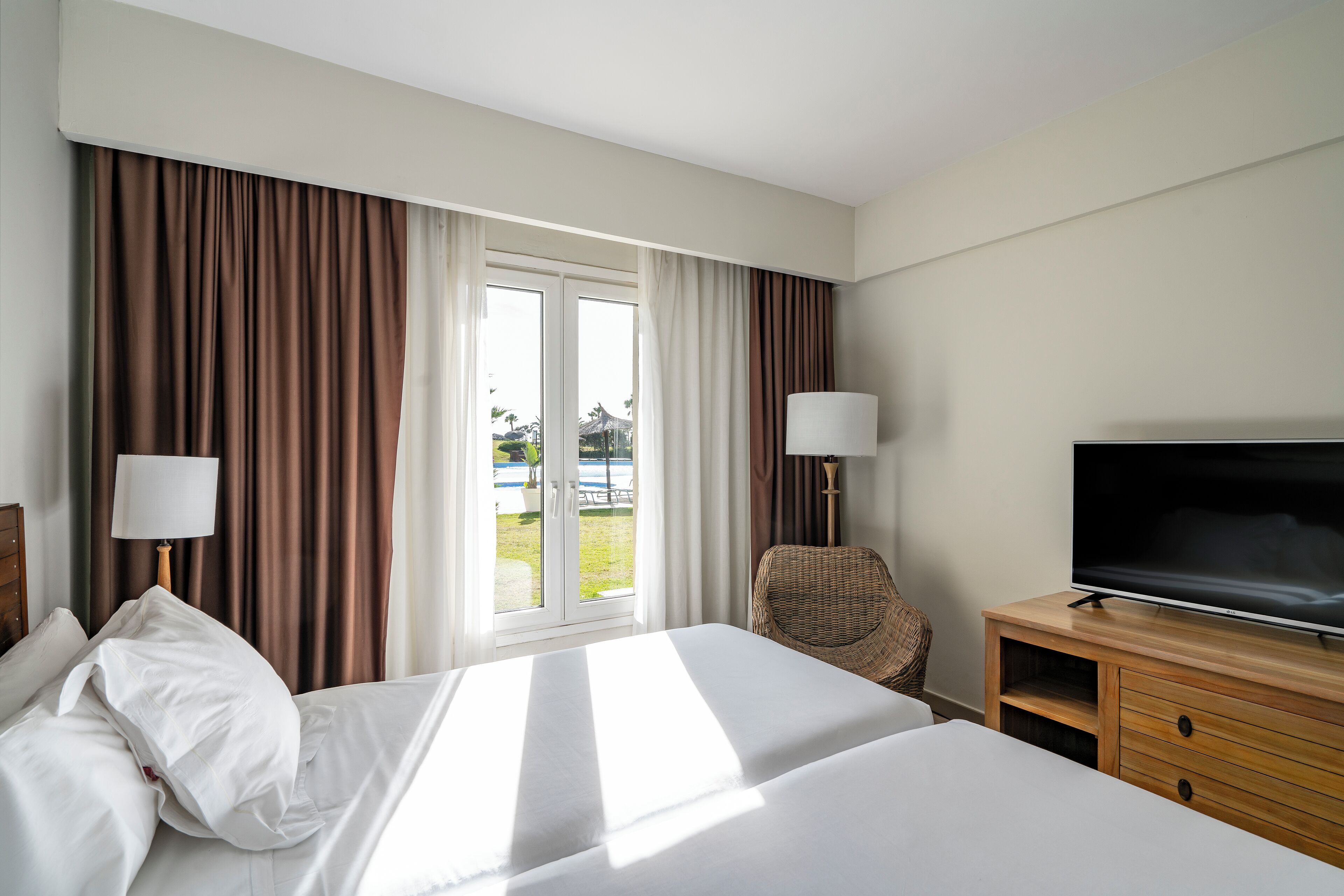Una habitación de hotel con cama, televisión, silla y ventana con cortinas.