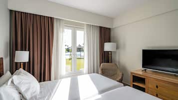 Quarto de hotel com cama, televisão, cadeira e janela com cortinas.
