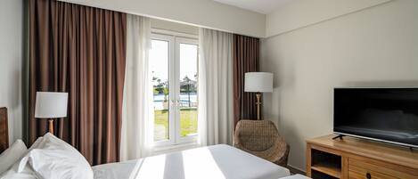 Una habitación de hotel con cama, televisión, silla y ventana con cortinas.