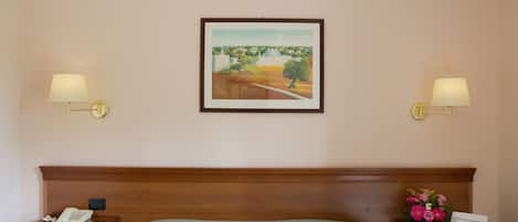 Una camera d'albergo con una testiera in legno, un letto con biancheria verde, due comodini con lampade, un telefono e un quadro con un paesaggio appeso al muro.