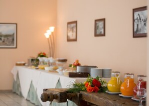 A breakfast table with a white tablecloth, plates, glasses, and a variety of food items. There are also three bottles of orange juice and a bouquet of flowers on the table. - Hotel Ramapendula (Alberobello)
