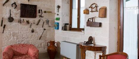 Una habitación rústica con pared de piedra, una silla de madera, una máquina de coser antigua y diversas herramientas colgadas en la pared.