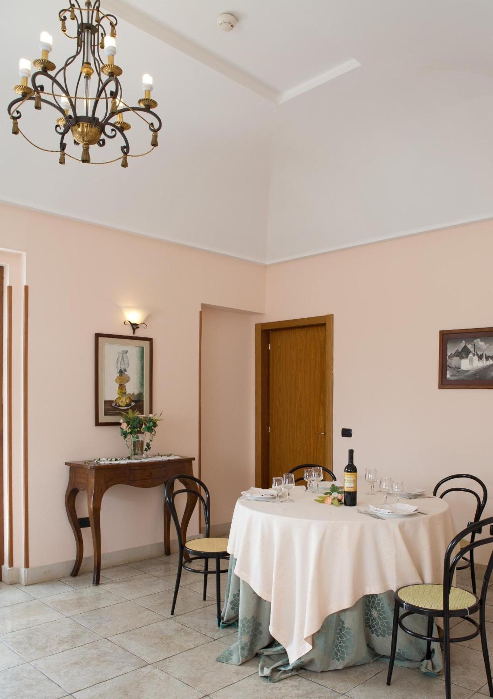A dining area with a round table set for four, a chandelier, a wooden sideboard, and a door.