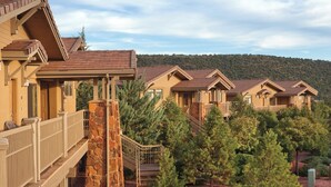 A row of modern, multi-story buildings with balconies and stone pillars, surrounded by landscaped gardens and trees.