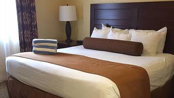A neatly made bed with white and brown linens, a striped pillow, and a brown accent pillow.