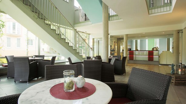 Um hall com uma mesa de mármore, cadeiras de vime, uma escadaria e um balcão de recepção.