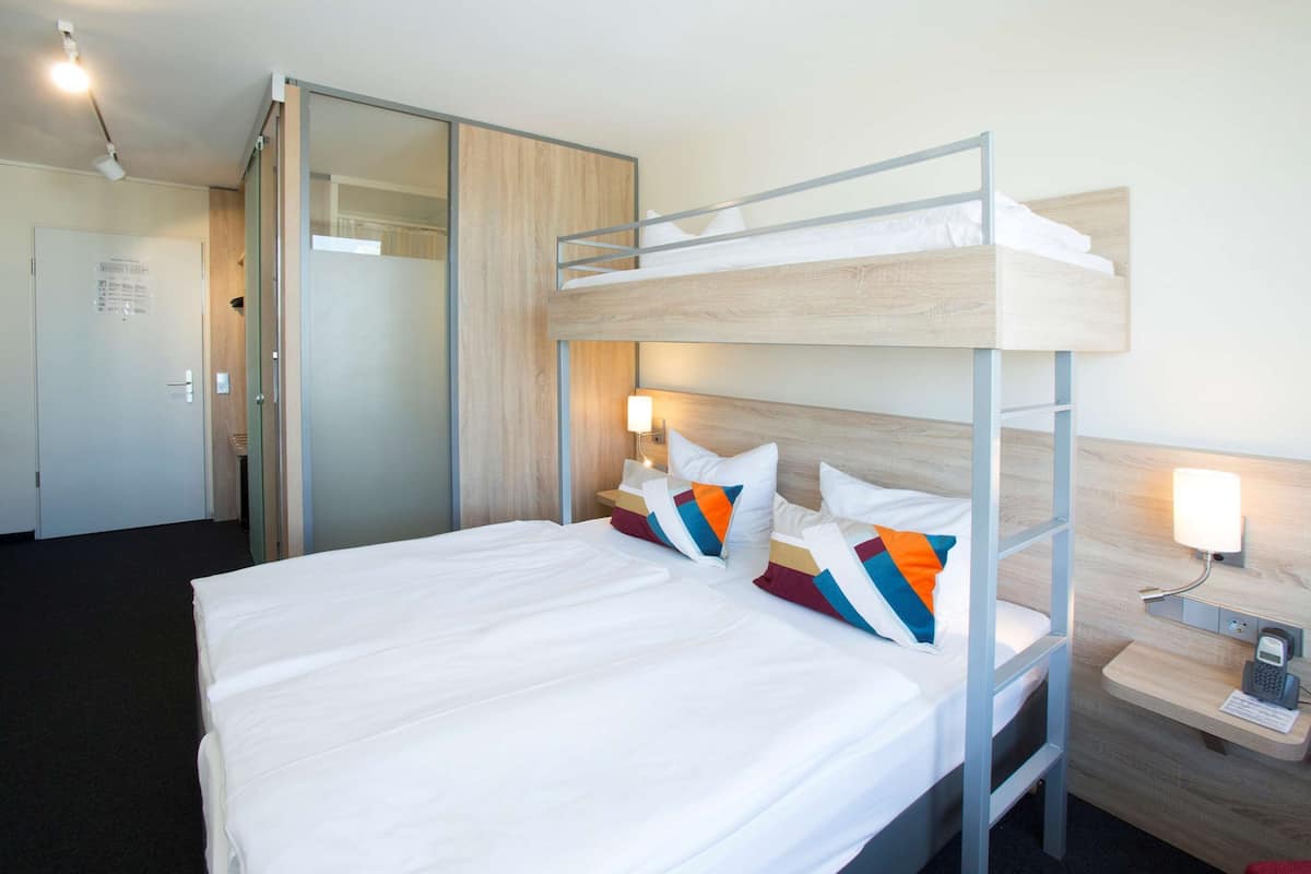 A bunk bed with white bedding and colorful pillows, a bedside table with a lamp, and a wooden headboard.